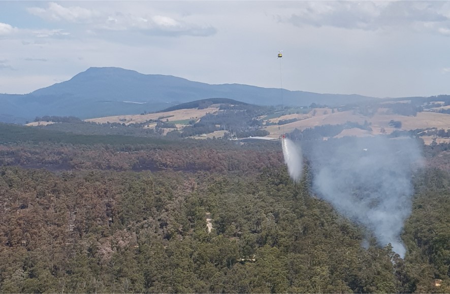 Figure 3: VH-UHX releasing the underslung bucket contents at a considerable height and distance away from the spot fire (smoke plume)