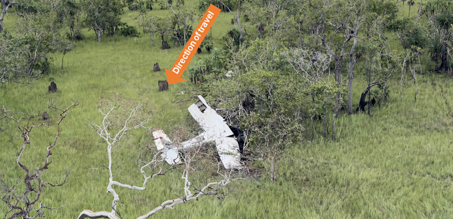 Photo of aircraft wreckage of Cessna 206 among trees, termite mounds and grass.