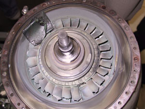 Second-stage gas-generator turbine blades damaged and oxidised, with one blade missing. Item in upper left corner is a guide vane from the power turbine NGV.