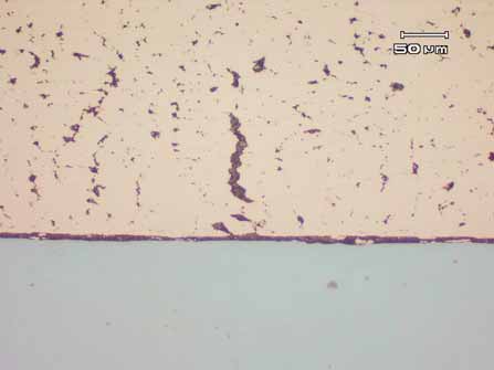 Figure 9. Cross-sectional microstructure of a damage bearing, showing the agglomeration of lead (dark phase) within the copper bearing alloy and along the backing interface. Unetched