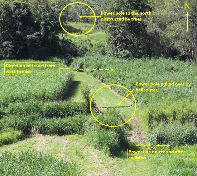 Figure 3: Terrain in the vicinity of the powerline, showing the helicopter’s direction of travel and the powerline and associated poles. Note the power pole that has been pulled down as a result of the wirestrike (centre of the picture) and the tree-lined creek that tracks right to left (located towards the top of the figure)