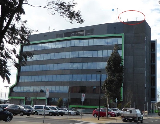 Figure 1: Hume City Council building showing the existing antennas (circled in red) and the (then) proposed radio mast (indicated with a blue arrow). Source: ATSB.