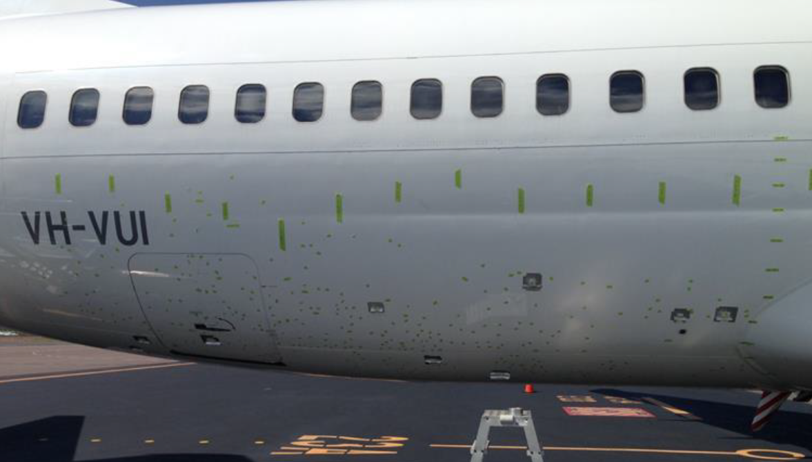 Figure 4: VH-VUI fuselage damage, marked with green tape. Image shows the locations of skin damage to the right side of the aircraft fuselage marked with short sections of tape on the underside of the fuselage. Longer sections of tape mark the locations of longitudinal and vertical fuselage reference lines. Source: Virgin Australia