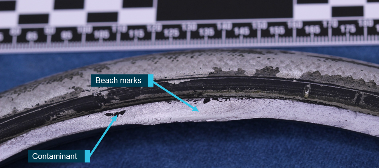 Figure 4: Magnified view of fatigue area showing crack progression along the bead seat and evidence of tyre contamination on the fracture surface.<br />
Source: ATSB