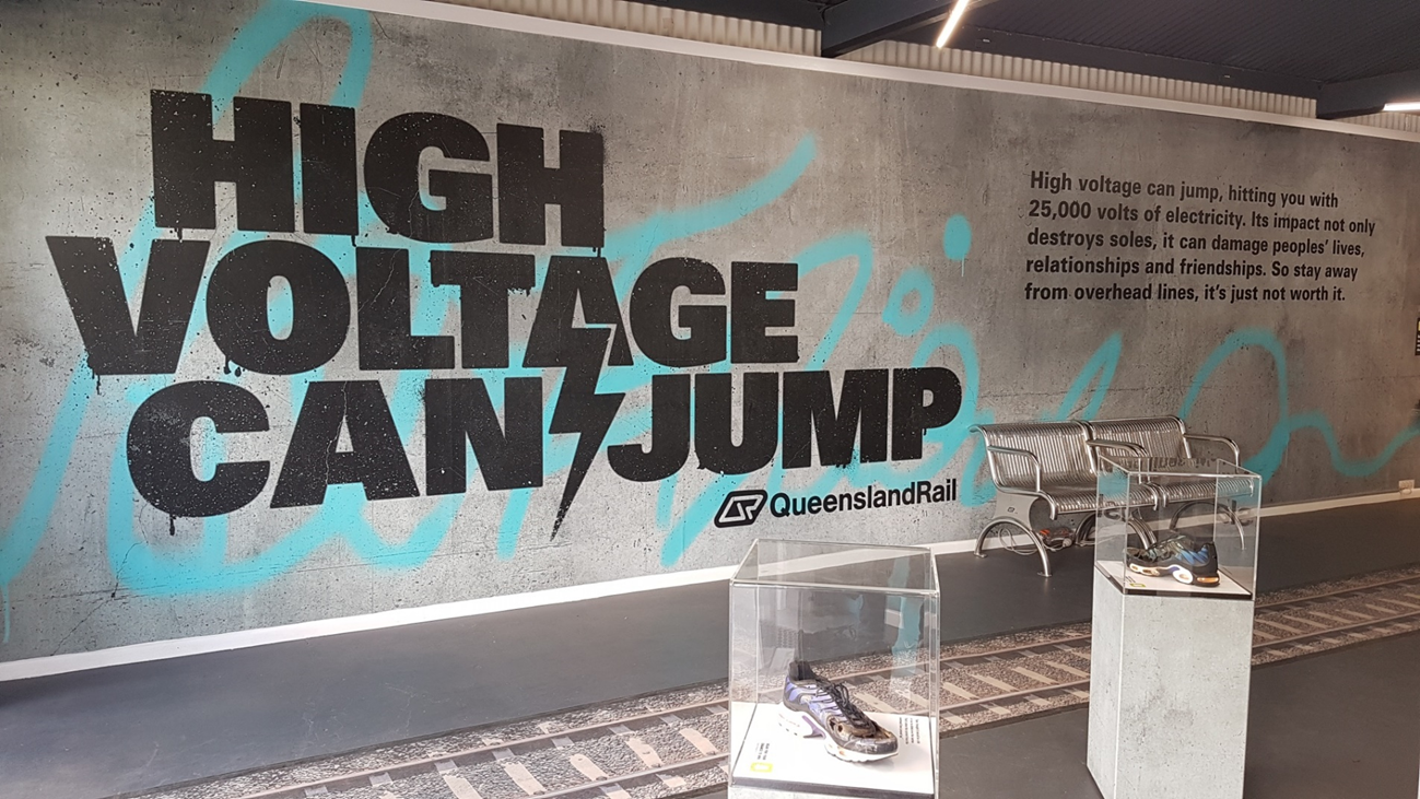 Figure A2: Queensland Rail’s ‘High Voltage Can Jump’ public awareness campaign.<br />
Image of Queensland Rail’s stand at the 2019 Brisbane Exhibition, highlighting the dangers of electrical arc from high voltage OHLE. The campaign was widespread throughout Brisbane, including significant display materials at Brisbane’s Central station.<br />
Source: ATSB