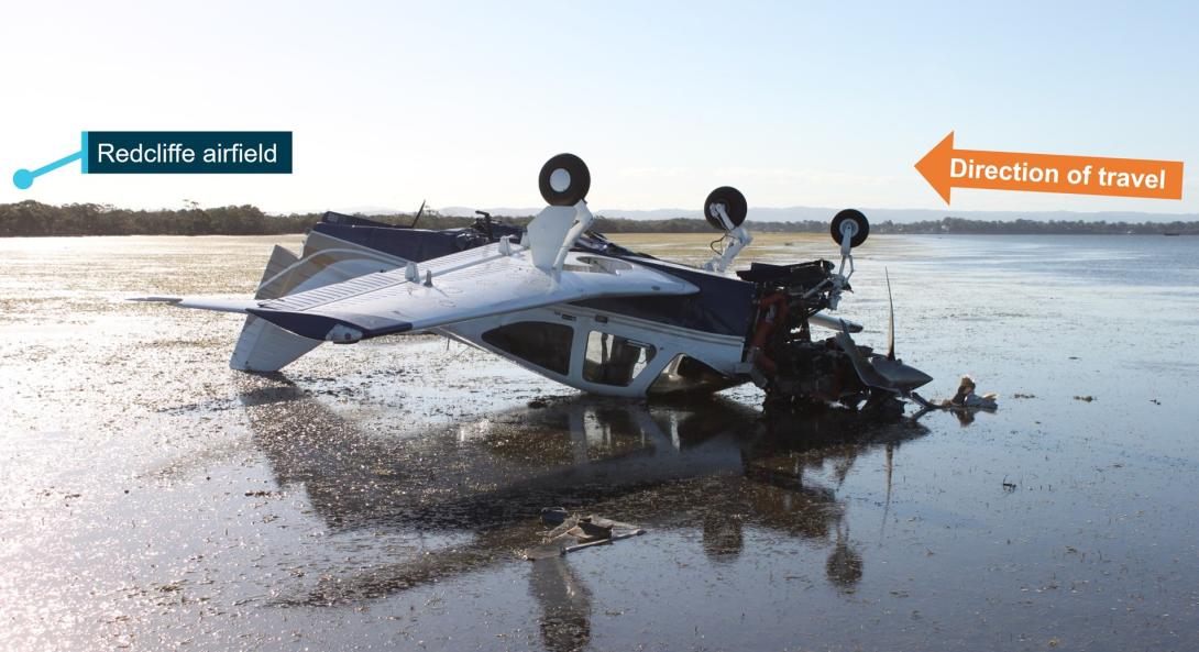 Accident site photo showing VH-WMM inverted on the tidal flat at low tide. The direction of travel and location of Redcliffe airfield are also noted.